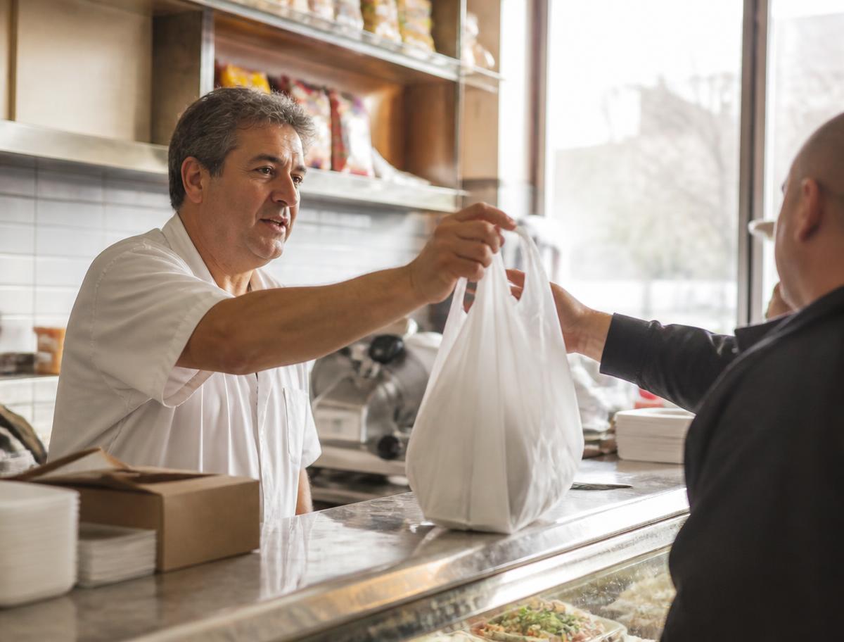 Neighborhood deli owner serving a customer at the counter of a New York shop
